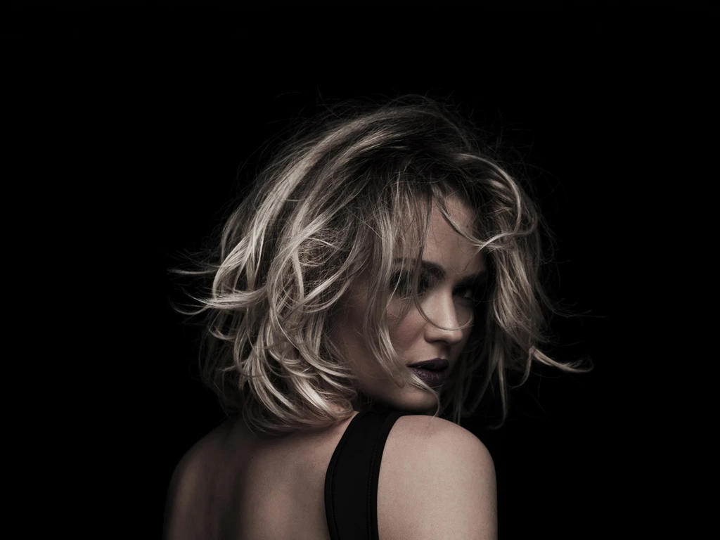 Glamorous studio portrait of a woman with tousled blonde hair looking over her bare shoulder, representing high-end aesthetic beauty at Marquis Plastic Surgery in Miami.